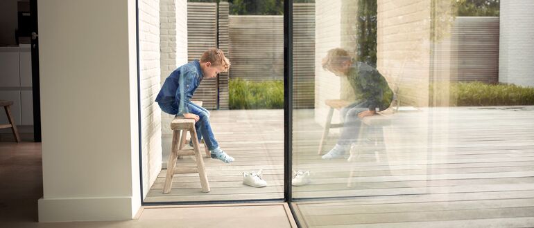 Boy on stool next to Reynaers Aluminium glass corner solution.