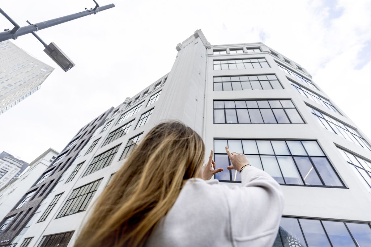 Mujer sosteniendo sus manos hacia un edificio blanco de mediana altura con muchas VENTANAS.