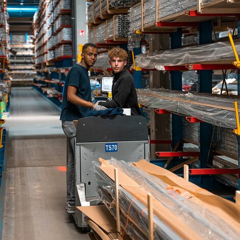 Two Reynaers co-workers transporting aluminium profiles in the warehouse.