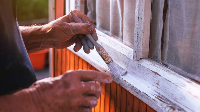 Man painting old wooden window frames white.