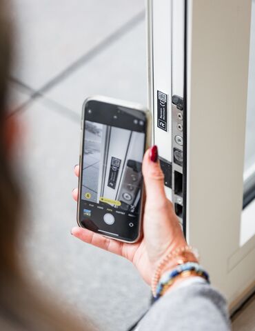 Mano sosteniendo un teléfono móvil cerca de código QR en una ventana con perfil blanco.