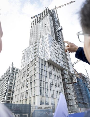 Hombre y mujer señalan un proyecto de gran altura de color gris en construcción.