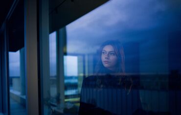 Mujer mirando por la ventana al anochecer.